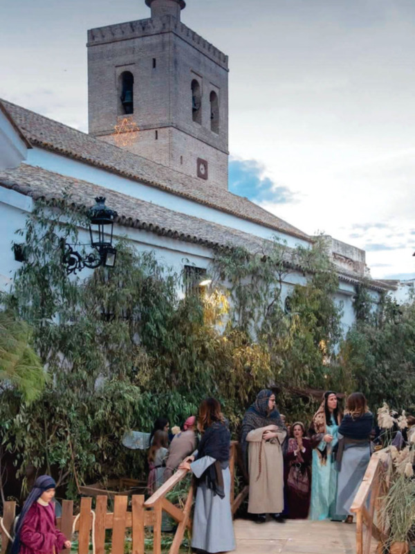 Una iglesia con una torre en el horizonte, rodeada de personas vestidas con vestidos antiguos, posiblemente en una celebración histórica o cultural.