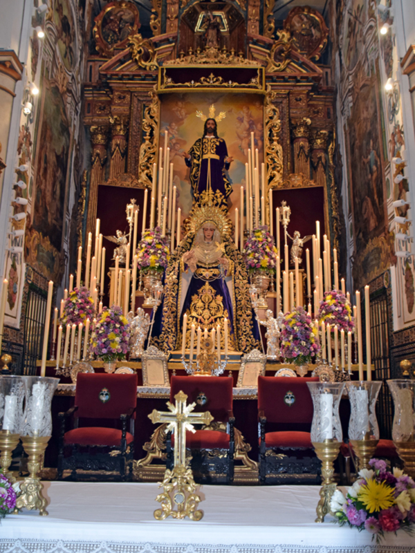 Interior de una iglesia con altares dorados, estatuas religiosas y flores.