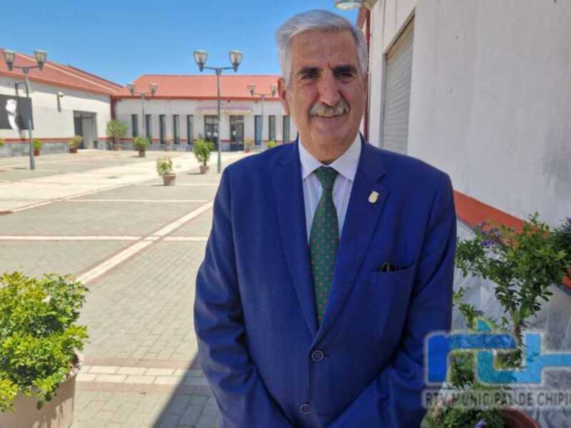 Un hombre en traje azul y corbata verde posa frente a una estructura de hormigón con plantas en el suelo.