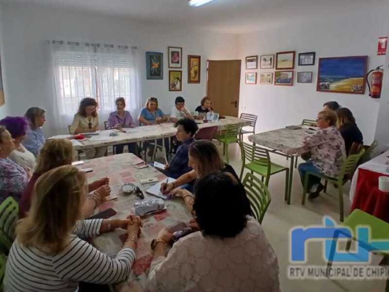 Gente reunida en una sala con mesas y sillas, probablemente en un evento o reunión.