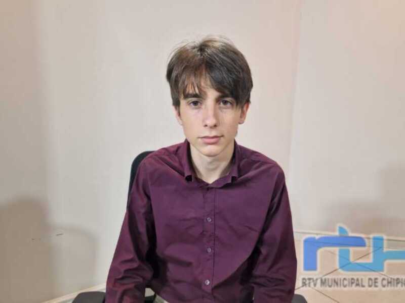 Un joven con cabello corto y una camisa de manga larga posando en un entorno interior.