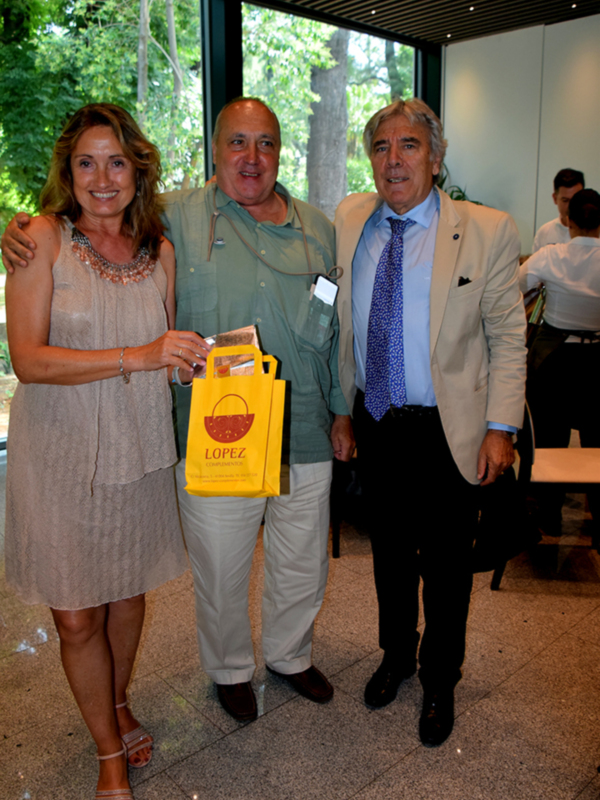 Tres personas sonrientes posan para una foto en un entorno interior, con uno de ellos sosteniendo un bolso amarillo con el nombre 'LOPEZ'.