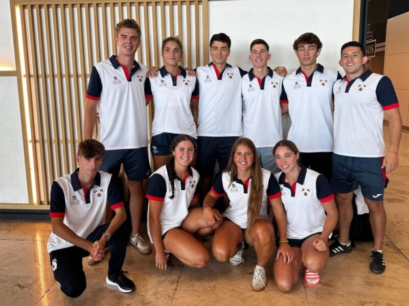 Equipo de atletas posando juntos en un gimnasio, todos vestidos con uniformes blancos y rojos.