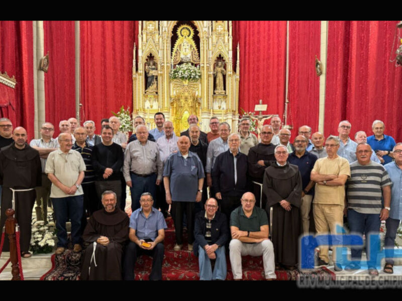 Grupos de hombres posan en una iglesia con arcos dorados y rojos, vestidos formalmente. Al fondo, se ve una imagen de la Virgen María en un altar dorado. La decoración incluye flores y velas, creando una atmósfera festiva.