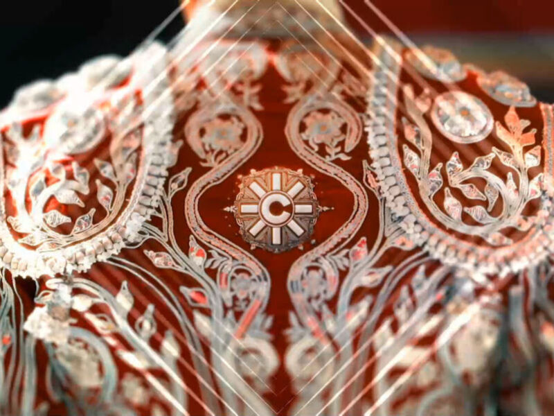 Detalle de una prenda bordada con motivos florales y geométricos en tonos rojos y blancos.