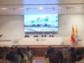 Presentación en el auditorio de la Universidad San Isidoro, con un panel de cuatro personas frente a una pantalla grande y banderas españolas.