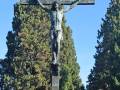 Escultura del Cristo crucificado en un cementerio, rodeado de árboles altos y verdes.