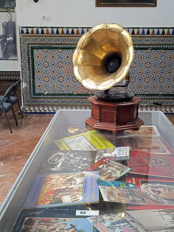 Un gramófono antiguo y una colección de postales antiguas en un mostrador, con una pintura de un hombre en la pared.